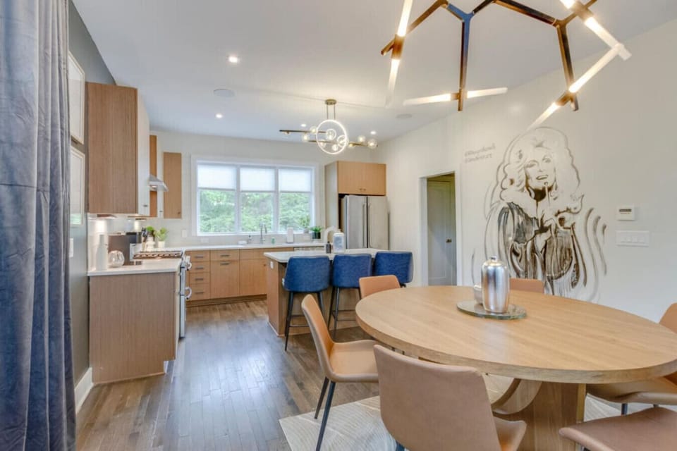 Dining room with abstract wall art mural, round table with chairs, and kitchen visible in background