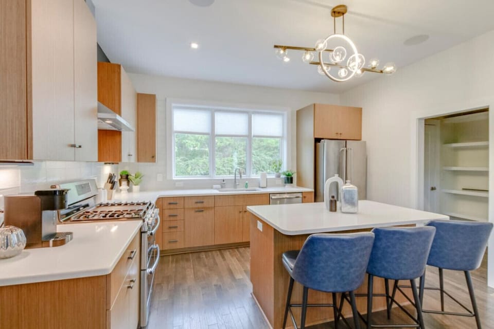 Kitchen with warm wood cabinetry, white quartz island, blue bar stools, and stainless appliances
