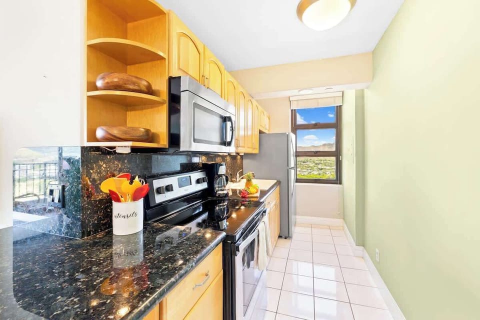 The full, well-equipped kitchen features granite countertops, warm wood cabinetry, and a window offering a glimpse of the scenic view.