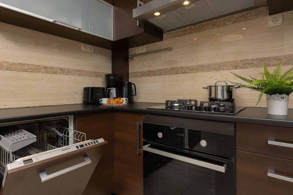 A modern kitchen with dark wooden cabinets, tiled backsplash, and built-in appliances. A dining table is set nearby.