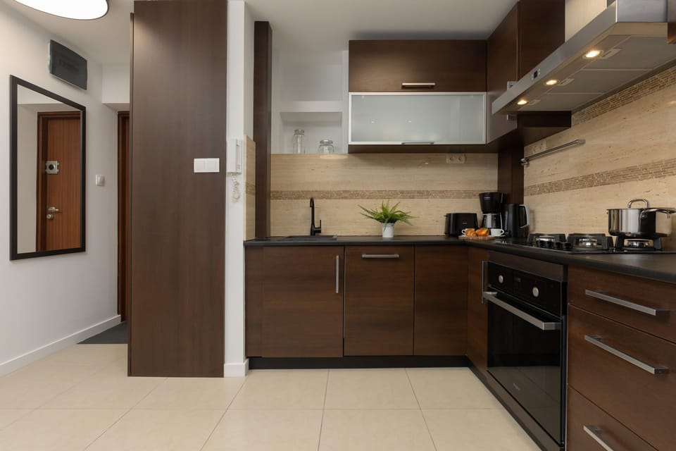A modern kitchen with dark wooden cabinets, tiled backsplash, and built-in appliances. A dining table is set nearby.