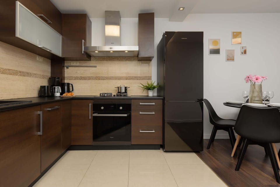 A modern kitchen with dark wooden cabinets, tiled backsplash, and built-in appliances. A dining table is set nearby.