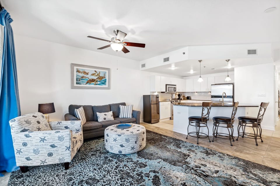 Open-concept living area with coastal-themed seating and a modern kitchen with bar stools.