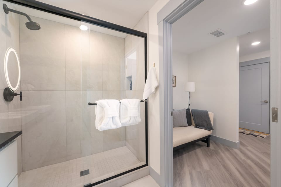 A modern bathroom with a glass shower enclosure, outside is a Twin sized futon for an extra guest