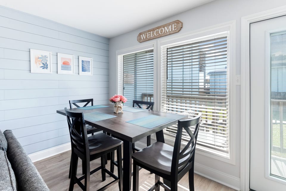Your bright dining nook welcomes meals with natural light streaming through plantation blinds and charming coastal decor.