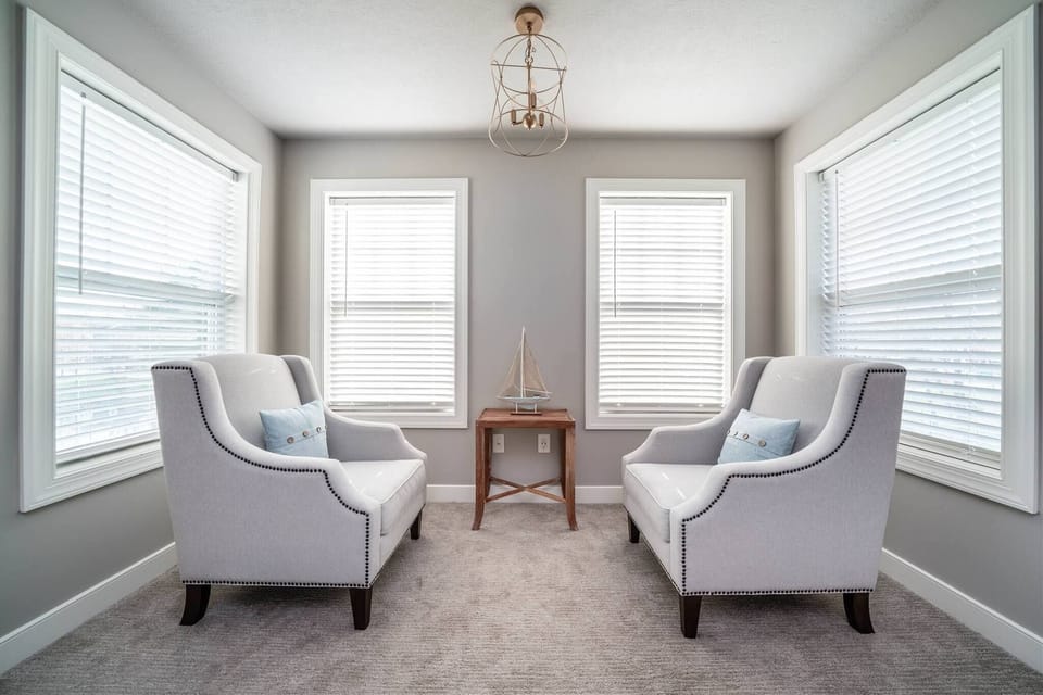 Escape to this serene sitting area featuring two plus armchairs, soft coastal pillows, and wraparound windows that fill the space with natural light.