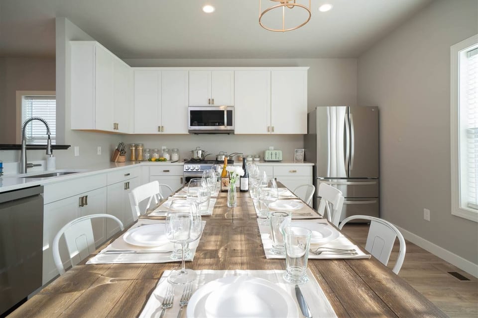 Gather and enjoy meals in this bright, modern kitchen featuring sleek white cabinetry, stainless steel appliances, and a spacious farmhouse-style dining table set for your entire group. With plenty of counter space and all the essentials.