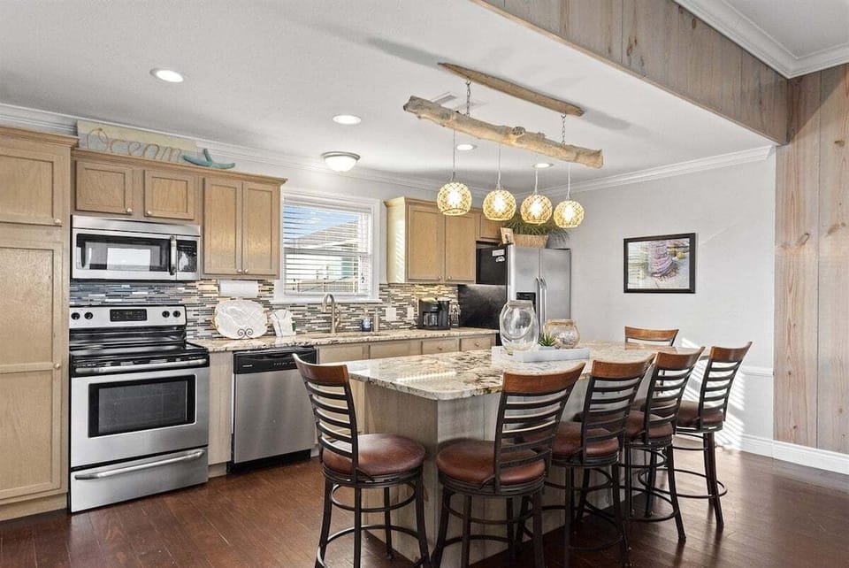 Kitchen close-up with stainless steel appliances, granite counters, pendant lights, and bright coastal cabinetry.