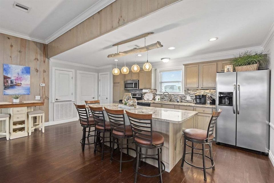 Island kitchen with granite breakfast bar, bar stools, stainless appliances, pendant lighting, and open dining flow.
