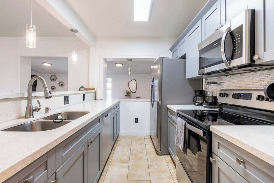 Fully-equipped Kitchen with a 4-seats countertop, dishwasher, blender, coffee maker, utensils, oven, microwave, refrigerator, pots, pans and a complete dinner set, including deep and flat plates, glasses, cups, and cutlery.