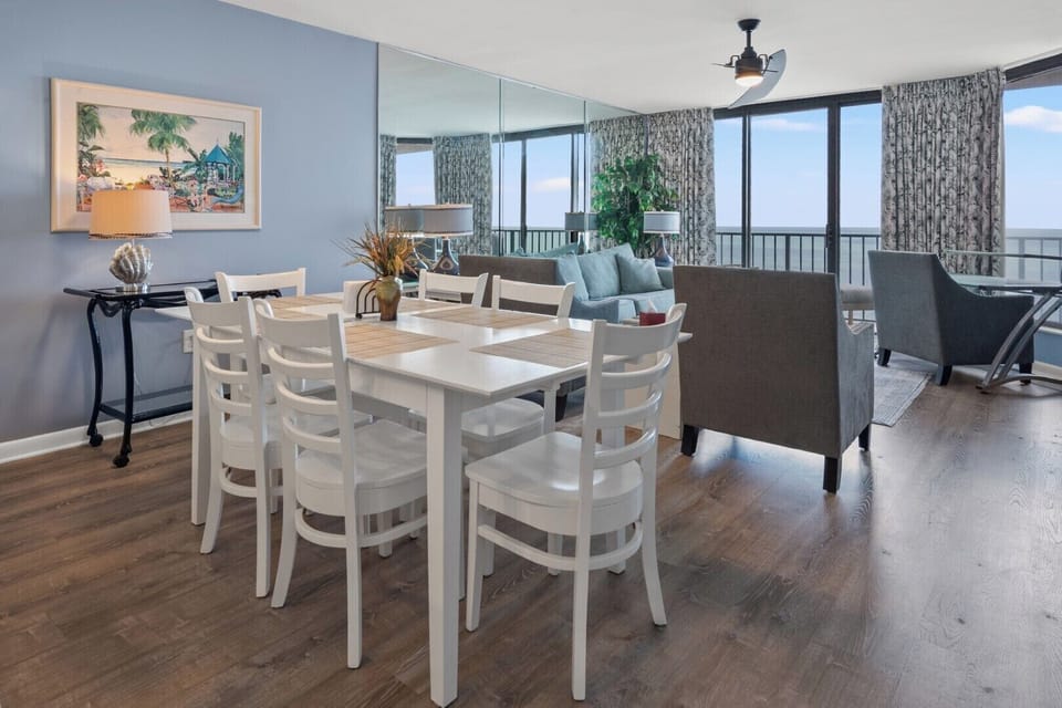 Dining table set beside wide ocean-view windows at Beach Club 2 9B, a Windy Hill vacation rental