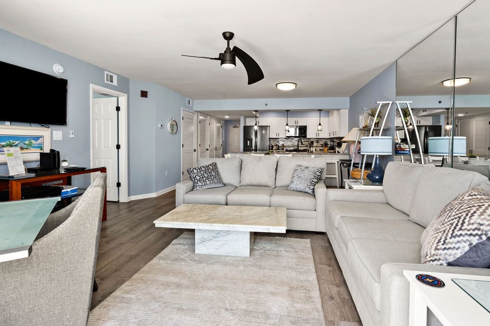 Soft blue living room with a wall-mounted TV and the kitchen beyond at Beach Club 2 9B, Windy Hill