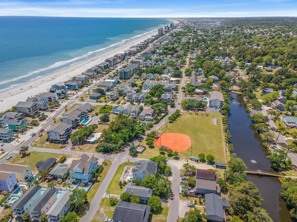 Aerial view of a charming coastal community with pristine beach, residential neighborhoods, and waterways creating an idyllic vacation destination setting.