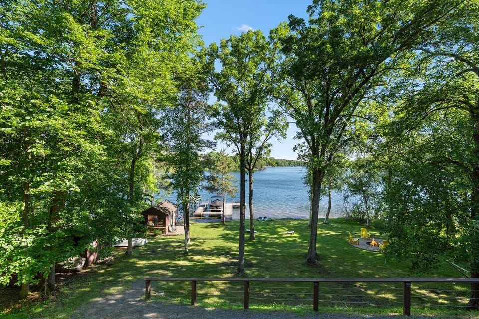 Scenic property set amid mature trees along a peaceful lake, featuring a private dock and expansive grassy grounds ideal for outdoor relaxation and activities.