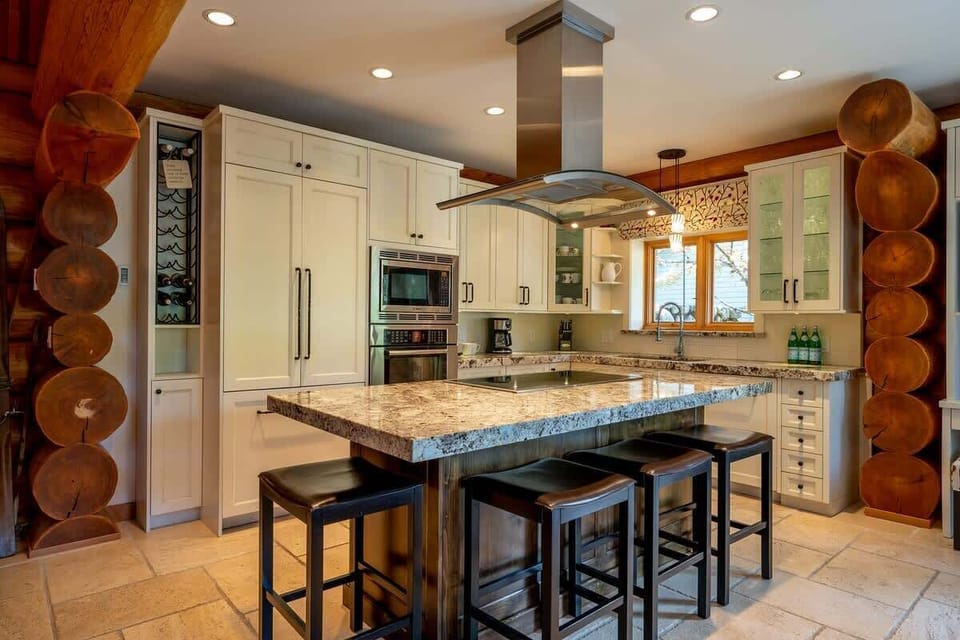 - Sleek cabin kitchen with granite island and stainless range hood  
- White cabinetry blends beautifully with rustic log accents  
- Perfect space for shared meals after Whistler ski adventures  
