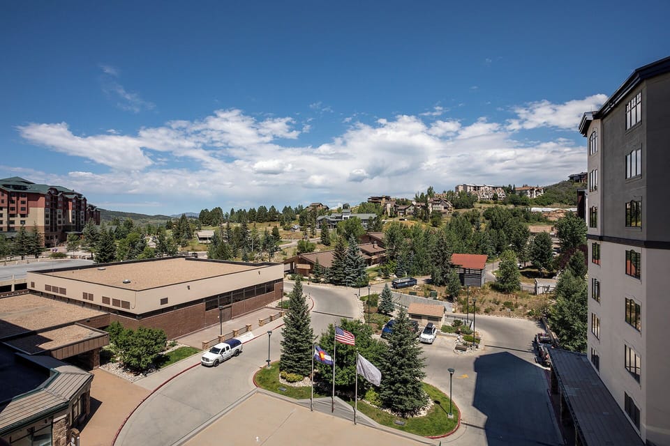 Scenic mountain community view showcasing the property's prime location amid rolling hills and neighboring buildings under expansive blue skies.