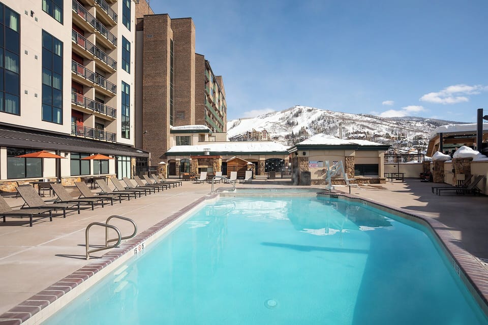 Property features an outdoor heated pool surrounded by lounge chairs, with direct ski slope access and stunning mountain views in the heart of the resort area.