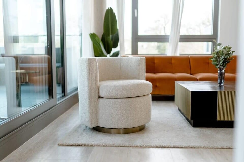 Bright lounge corner with a cozy swivel chair and large windows, offering a peaceful spot to unwind or read