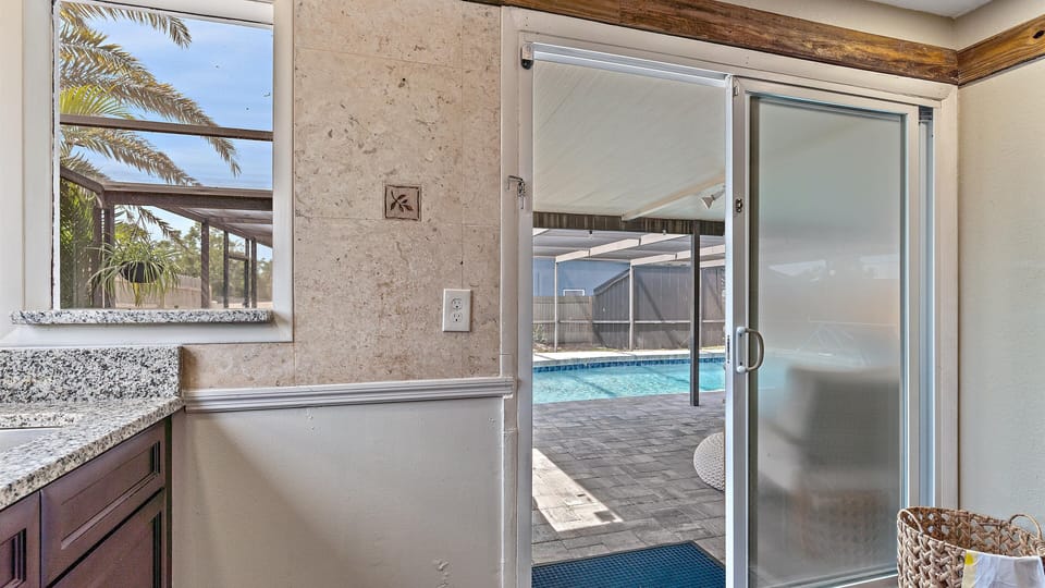 A pool view from an interior space with a sliding glass door; outside, there's a screened patio, paving stones, and a swimming pool.