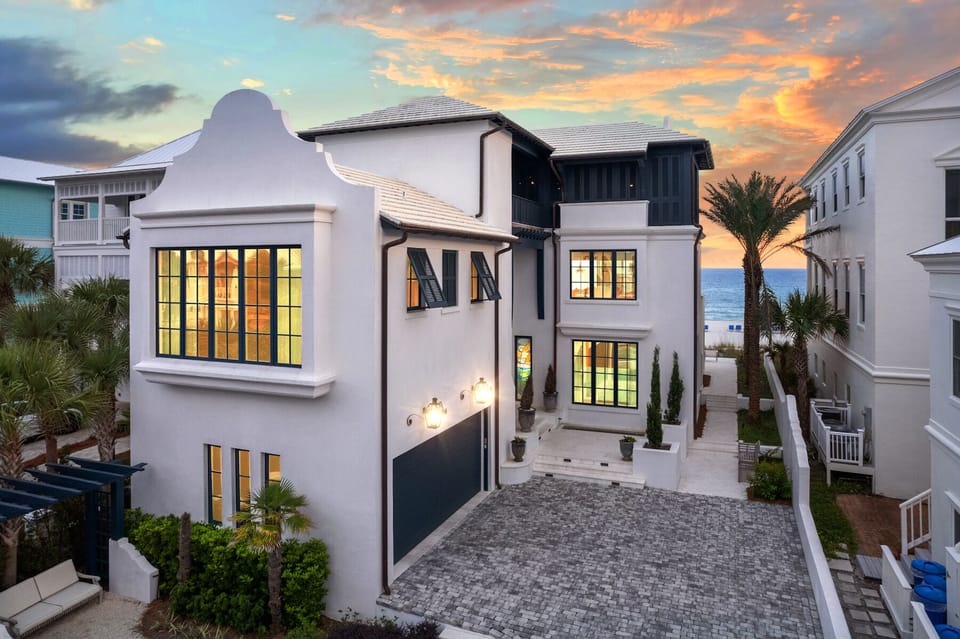 Stunning beachfront property featuring elegant architecture and tropical landscaping, perfectly positioned near the shore with dramatic sunset skies overhead.