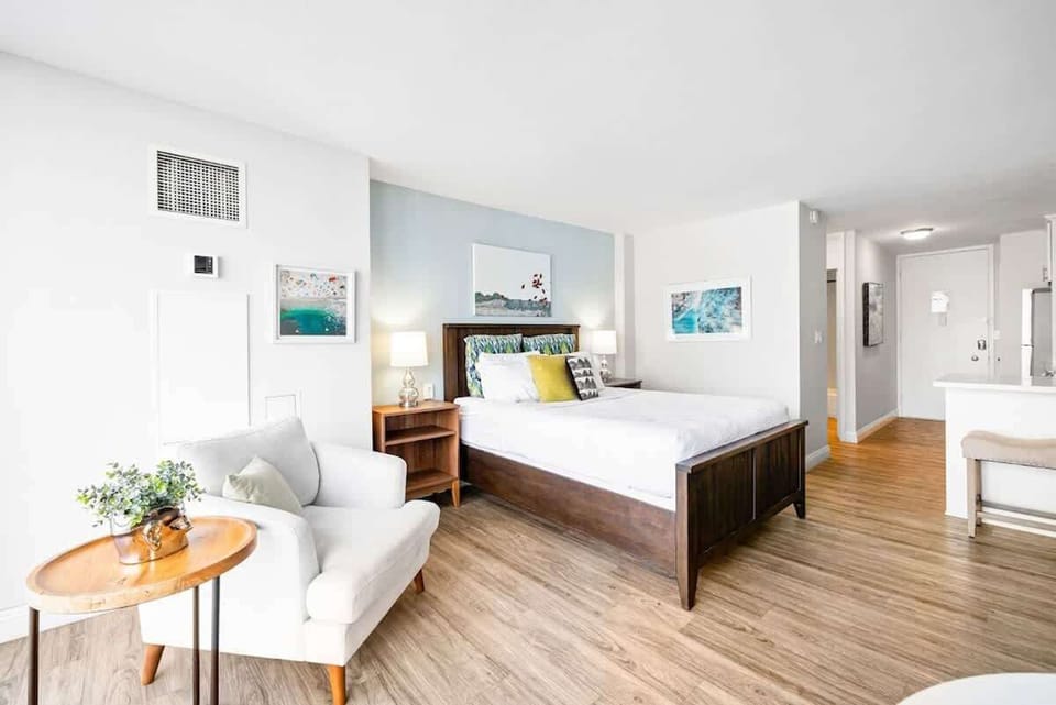 Bright studio with a queen bed, chair and a cute table