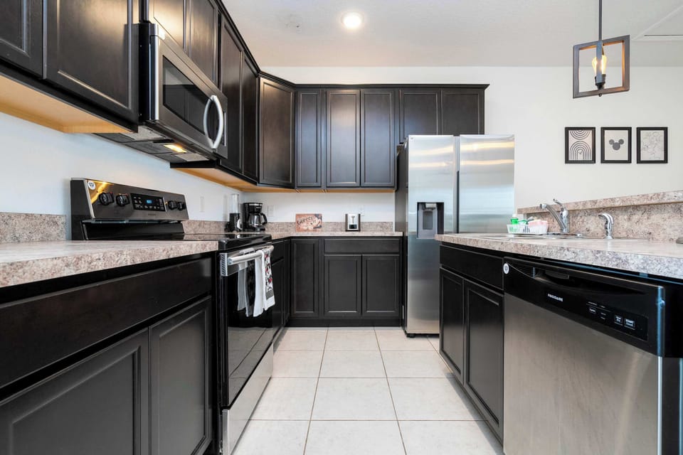 Cook with ease in this sleek, modern kitchen-dark shaker cabinets, stainless appliances, and a breakfast bar with pendant lights for ample prep space.