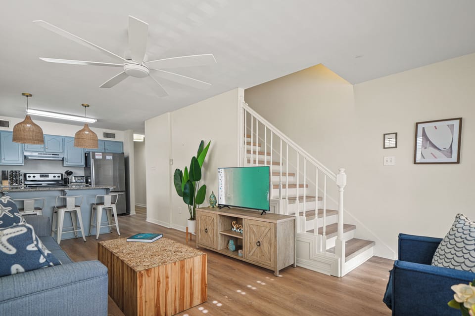 Unit A main living area, highlighting the open layout with the kitchen and staircase to upper levels. Comfortable seating and a TV create a welcoming space for relaxing and gathering.