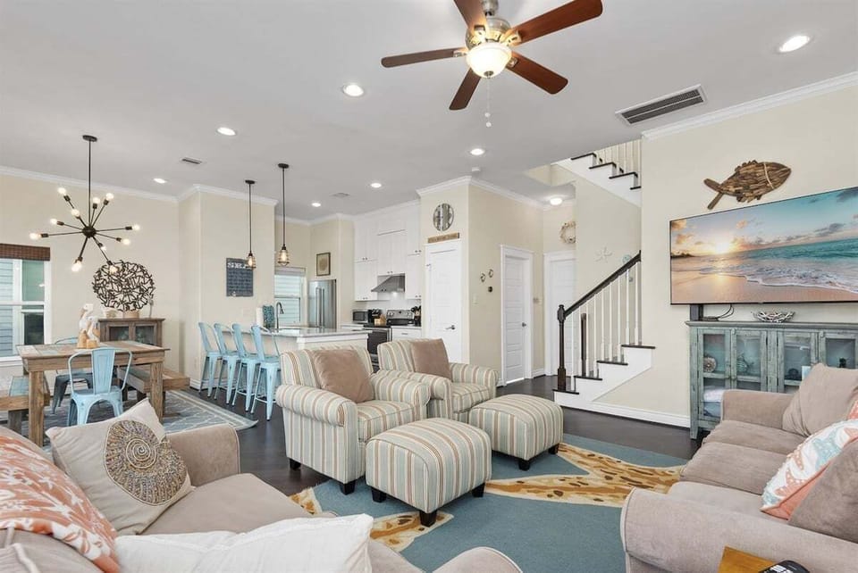 Spacious living area with comfortable seating, beach-inspired décor, ceiling fan, and open layout connecting to kitchen and dining spaces.
