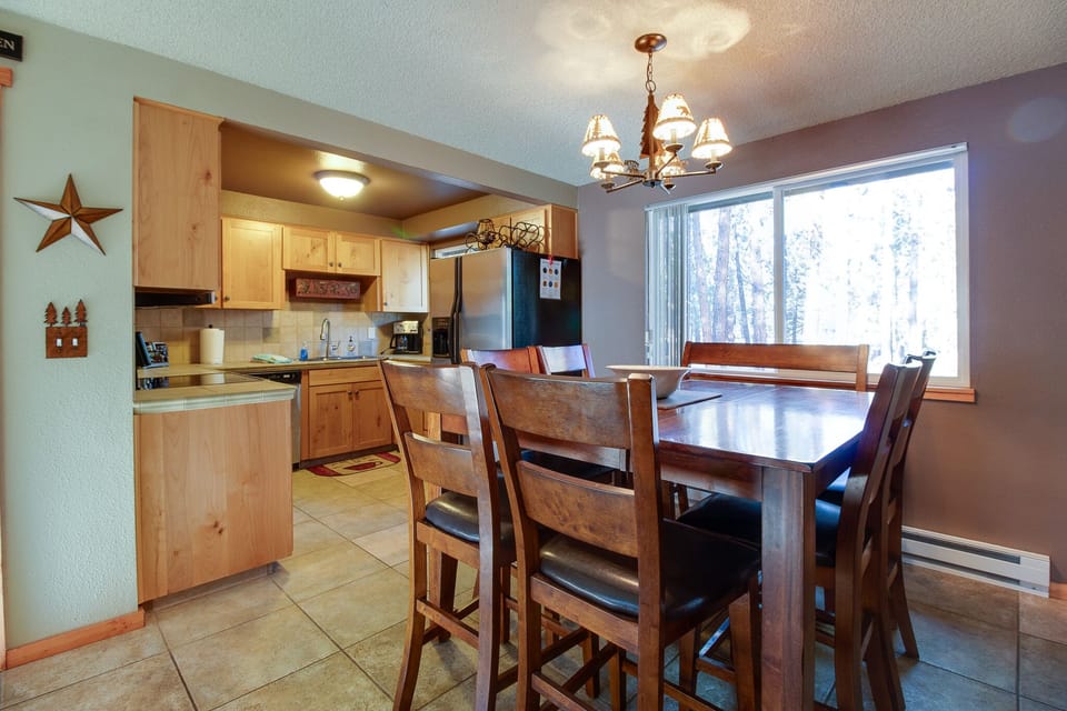 Gather around this inviting dining table with forest views streaming through the large window, perfect for your morning coffee or evening meals in the fully equipped kitchen.
