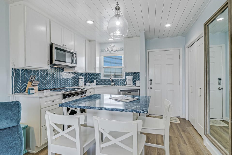 Your coastal kitchen awaits with blue herringbone backsplash, granite island, and white coastal charm perfect for morning coffee or dinner prep.