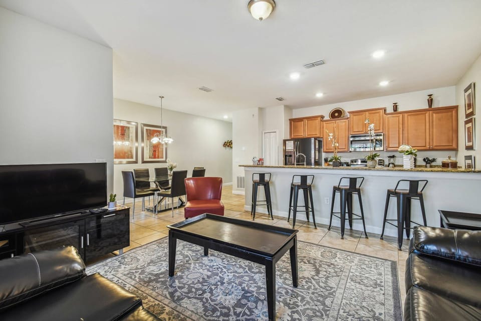 Welcome to a bright, spacious living area featuring a cozy black leather sofa and a chic red armchair. The modern kitchen boasts warm wood cabinetry and sleek bar seating, perfect for casual dining and entertaining.