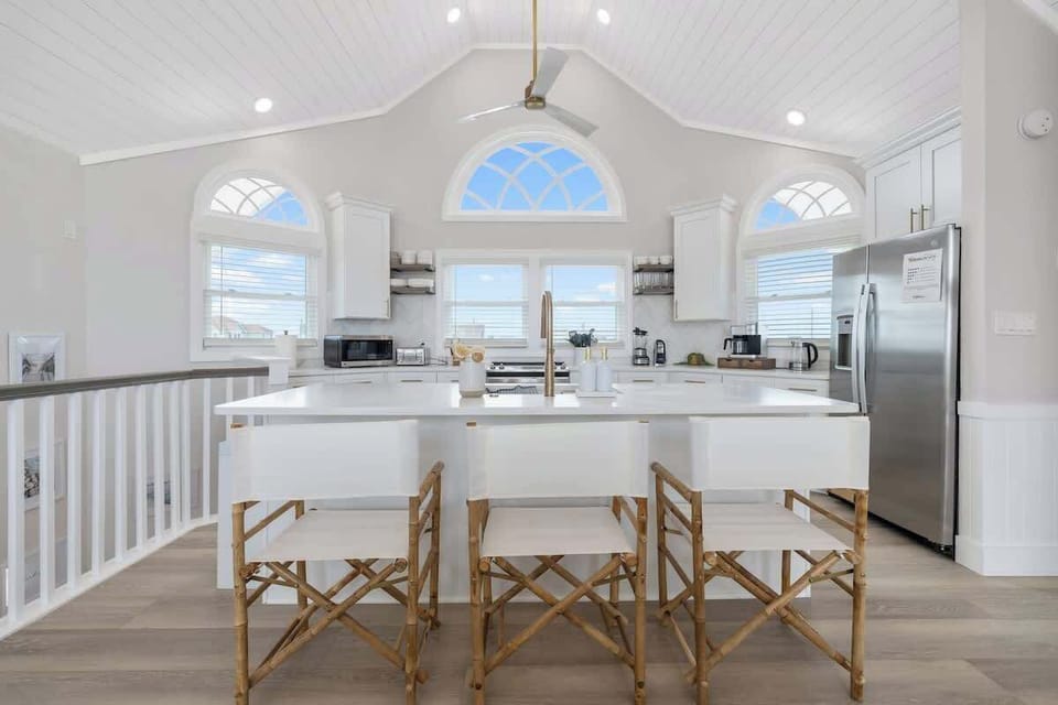 Nicely equipped kitchen with vaulted ceilings has refrigerator, stove, microwave dishwasher, blender, Keurig coffee maker, toaster, pots and pans, plates, glasses, wine glasses, coffee cups, cooking and eating utensils.