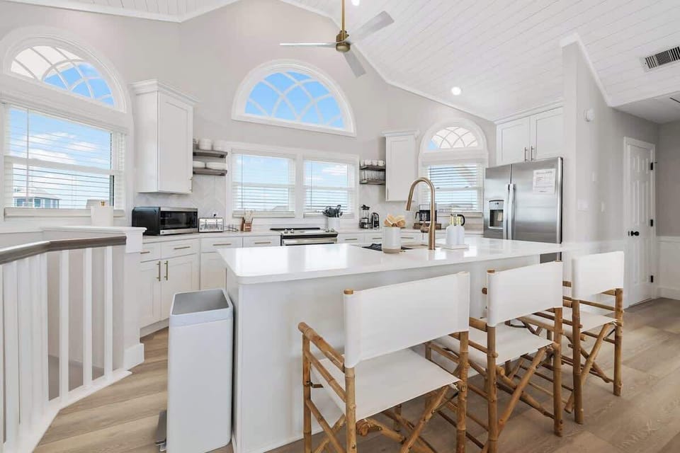 Nicely equipped kitchen with vaulted ceilings has refrigerator, stove, microwave dishwasher, blender, Keurig coffee maker, toaster, pots and pans, plates, glasses, wine glasses, coffee cups, cooking and eating utensils.