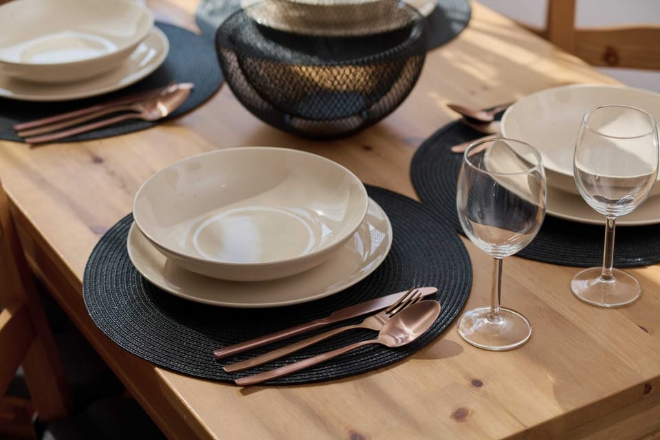 A close-up of a dining table set with elegant black and white plates, silverware, and wine glasses. 