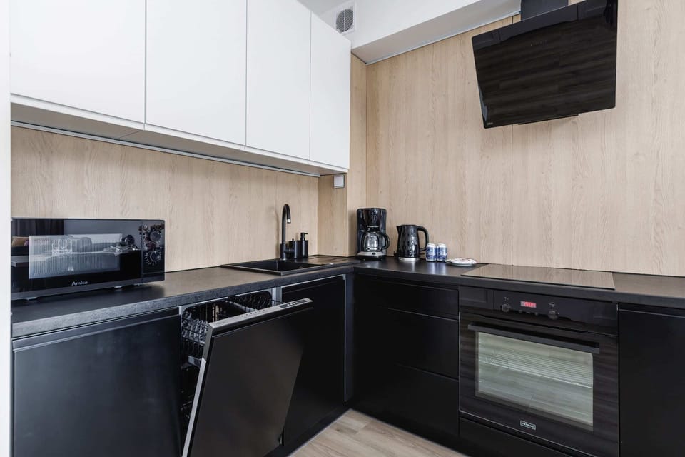 A compact kitchen with modern appliances, including a coffee maker and an electric kettle, on a light wood countertop.