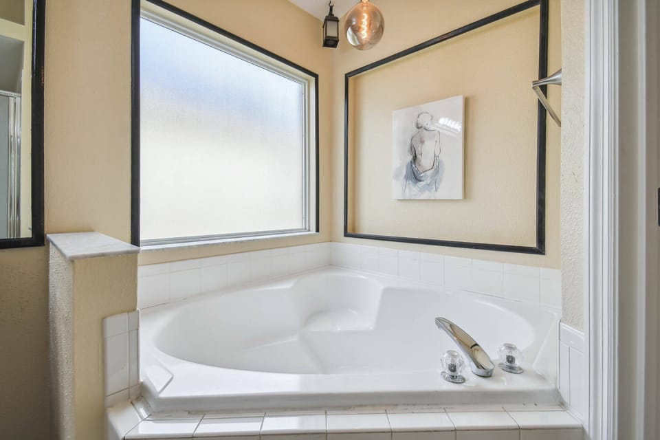 Relax in the spacious corner jetted tub, where soft natural light filters through large windows. The elegant black trim and tasteful artwork create a calming atmosphere, making this bathroom a true oasis for your comfort.