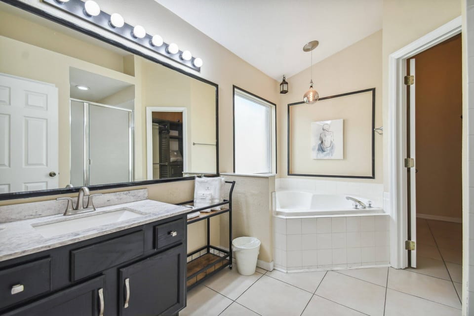Discover this bright, airy bathroom with a spacious dual vanity and dark cabinetry. Large windows flood the space with natural light, highlighting the elegant soaking tub and stylish decor for your ultimate comfort.
