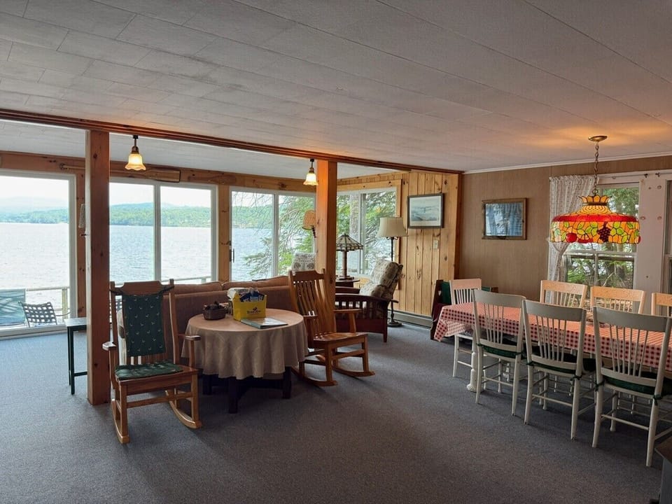 Picture yourself relaxing in this welcoming lakeside retreat, where large windows frame stunning water views and cozy rocking chairs invite you to unwind. Your dining table awaits with warm lighting and comfortable seating for shared meals.