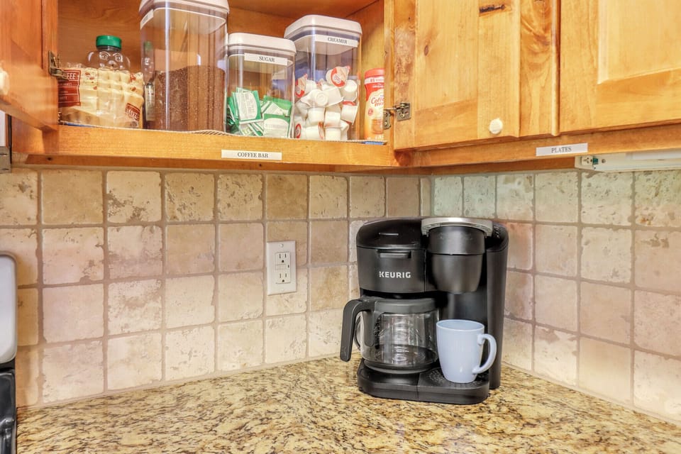 Your own coffee bar awaits, stocked with essentials and a Keurig ready to brew your perfect morning cup in this thoughtfully organized kitchen corner.