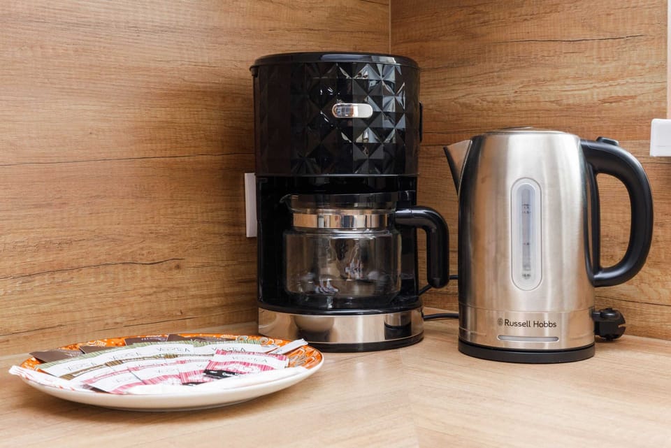 A coffee maker, kettle, and mugs placed on the countertop, emphasizing the homely amenities.