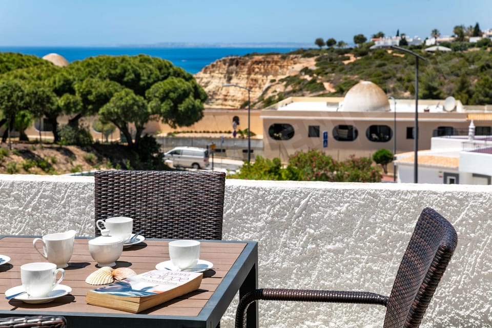 Relax on the sunny terrace at Apartment Centeanes with morning coffee and sea views. The outdoor dining area features comfortable wicker seating, perfect for enjoying the Algarve sunshine.