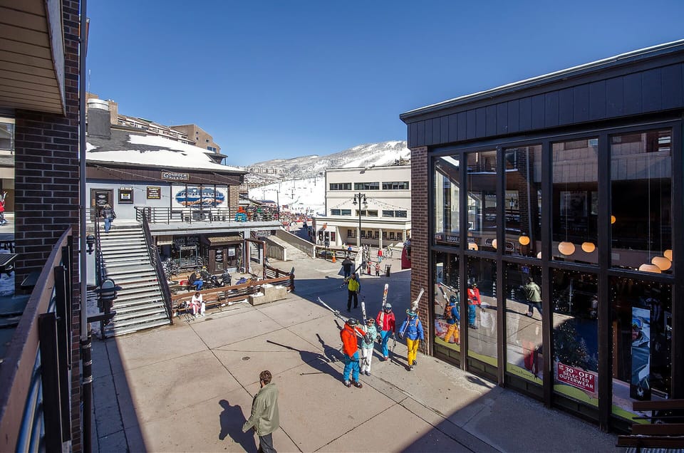 Vibrant ski village plaza with mountain shops, dining, and snow-capped peaks creating an alpine adventure atmosphere.