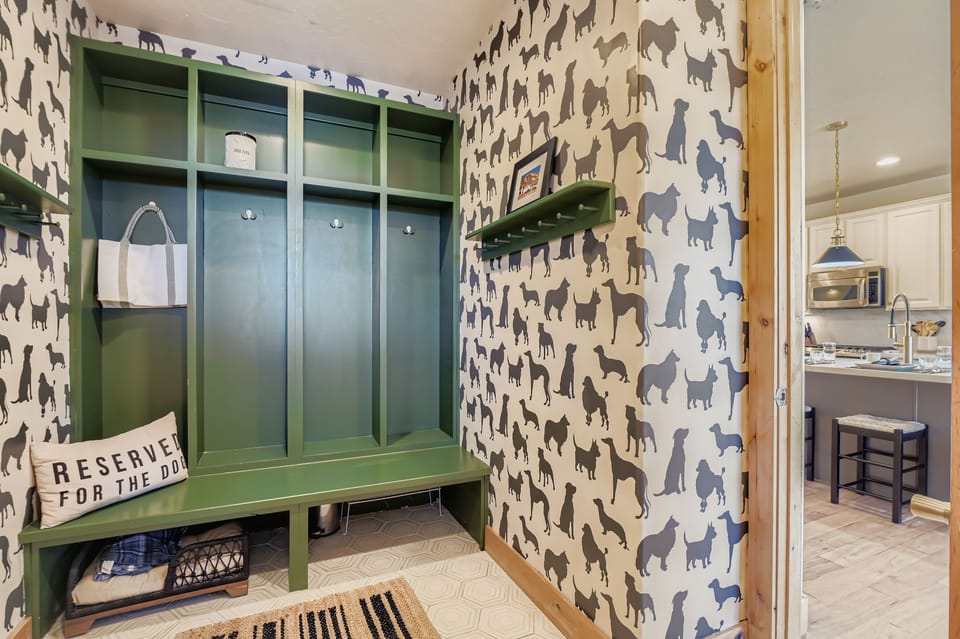 This playful dog-themed mudroom features custom green cabinetry and whimsical "Dog Flock" wallpaper. A built-in bench and high shelving provide stylish, organized storage for pet gear and outdoor essentials.