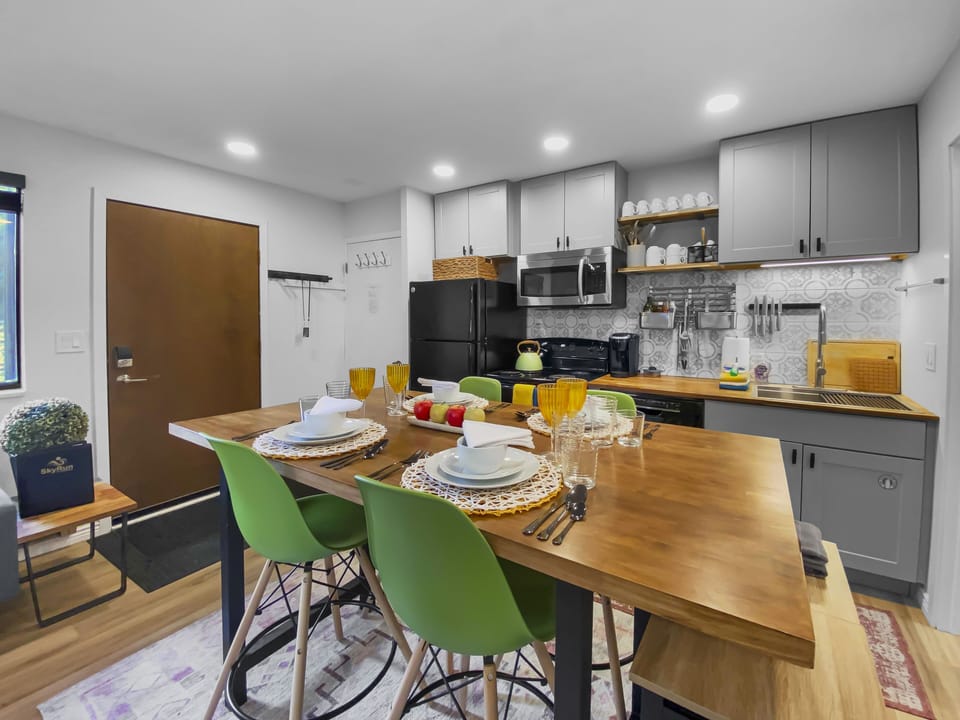 Dine in style or relax! This inviting space features a modern wooden dining table with vibrant green chairs, an open-plan living area, and easy access to the patio.