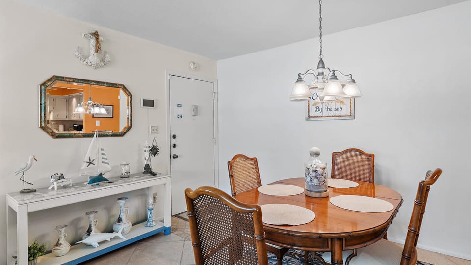A dining room with a round wooden table set for four, nautical-themed decorations, a console table with coastal ornaments, and a white pendant light hanging above.