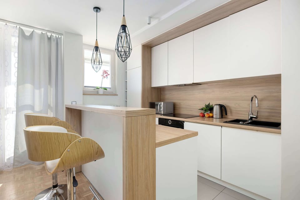 A bright kitchen area with a breakfast bar and wooden stools. White cabinetry contrasts with warm wood textures.