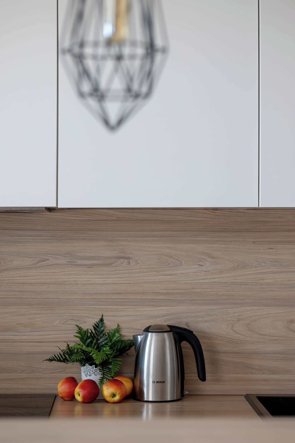A close-up of a kitchen counter with a kettle and small decorative items. Simple accessories add warmth to the clean design.