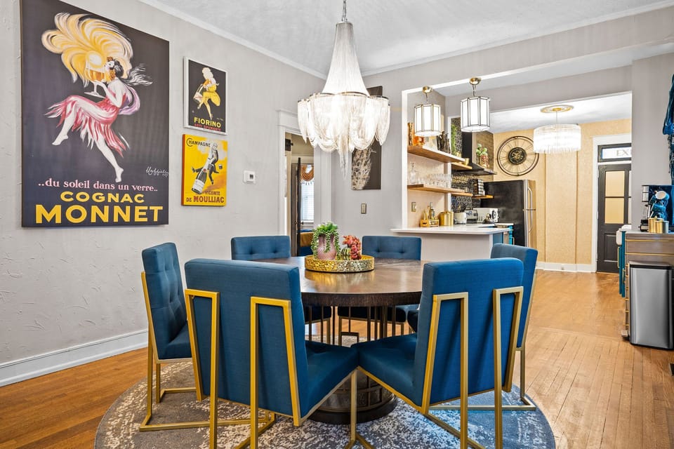 Gather around the lower-level Art Deco dining space featuring plush blue seating, a modern round table, and vintage poster décor—perfect for group meals during your Midtown Kansas City stay.