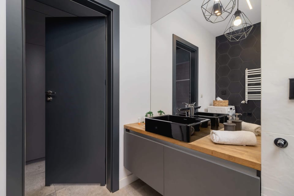 A compact bathroom with a washer, black tile walls, and a heated towel rack, combining style and practicality.
