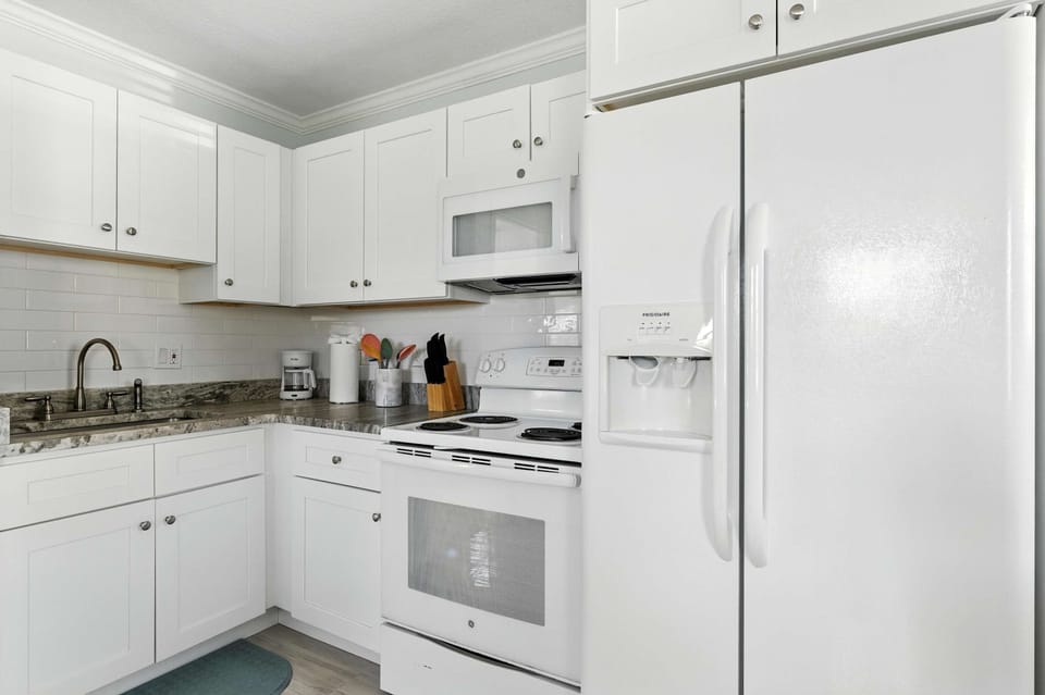 Bright, fully equipped kitchen with sleek white cabinetry, modern appliances, and granite countertops. Perfect for cooking up your favorite meals while enjoying the clean, fresh coastal vibe of your getaway.